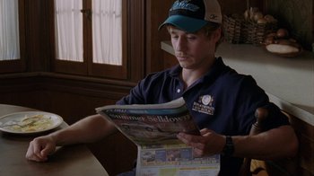 Movie still from “Junebug” (2005), directed by Phil Morrison – A man reading a newspaper while sitting at a table; Close Up shot, High angle