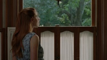 Movie still from “Junebug” (2005), directed by Phil Morrison – A woman standing on a porch looking out a window; Medium shot, Over the shoulder angle