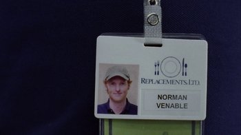 Movie still from “Junebug” (2005), directed by Phil Morrison – A name tag with a picture of a man in a hat; Extreme Close Up shot, Overhead angle