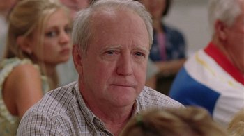 Movie still from “Junebug” (2005), directed by Phil Morrison – An older man sitting in front of a group of people; Close Up shot, Over the shoulder angle
