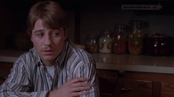 Movie still from “Junebug” (2005), directed by Phil Morrison – A man sitting on a counter in front of jars; Close Up shot, Over the shoulder angle