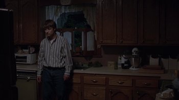 Movie still from “Junebug” (2005), directed by Phil Morrison – A man standing in a kitchen next to a counter; Wide shot, Low angle