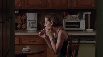 Movie still from “Junebug” (2005), directed by Phil Morrison – A woman sitting at a table with a cigarette in her mouth; Medium shot, Over the shoulder angle