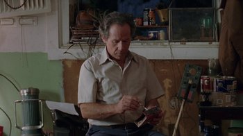Movie still from “Junebug” (2005), directed by Phil Morrison – An older man sitting in a chair holding a pair of scissors; Medium shot, High angle