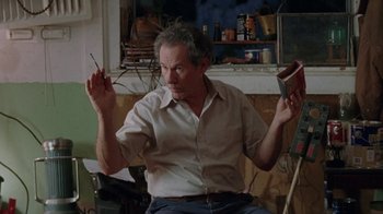 Movie still from “Junebug” (2005), directed by Phil Morrison – An older man sitting in front of an open book; Medium shot, Low angle