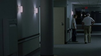 Movie still from “Junebug” (2005), directed by Phil Morrison – A man standing in a room with a light on the wall; Wide shot, Over the shoulder angle