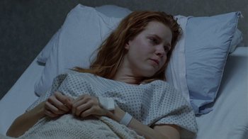 Movie still from “Junebug” (2005), directed by Phil Morrison – A woman laying in a hospital bed with a bandage on her arm; Medium shot, Low angle