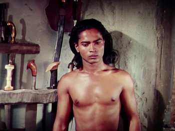 Movie still from “The Jungle Book” (1942), directed by Zoltan Korda – A shirtless man standing in front of a table with tools; Medium shot, Low angle