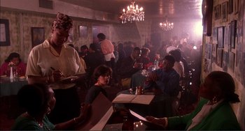 Movie still from “Jungle Fever” (1991), directed by Spike Lee – A group of people sitting at tables in a room; Medium shot, High angle