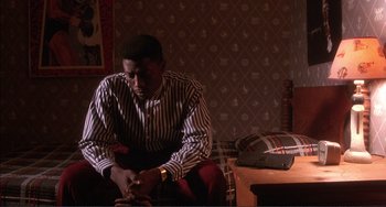 Movie still from “Jungle Fever” (1991), directed by Spike Lee – A man sitting on a chair in a room; Medium shot, High angle