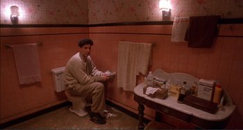 Movie still from “Jungle Fever” (1991), directed by Spike Lee – A man sitting on top of a toilet in a bathroom; Wide shot, High angle