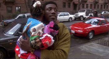 Movie still from “Jungle Fever” (1991), directed by Spike Lee – A man holding a child on a street; Close Up shot, Over the shoulder angle