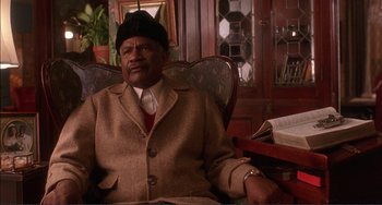 Movie still from “Jungle Fever” (1991), directed by Spike Lee – An older man sitting in a chair in a room; Medium shot, Low angle