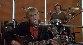 Movie still from “Just My Luck” (2006), directed by Donald Petrie – A man singing into a microphone in front of another man in a drum set; Medium shot, Low angle