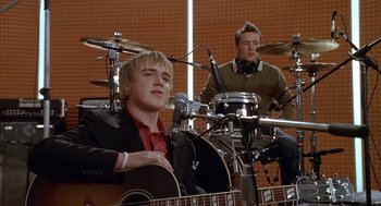 Movie still from “Just My Luck” (2006), directed by Donald Petrie – A man sitting in front of a microphone and a guitar; Medium shot, Low angle