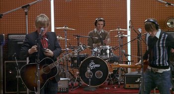 Movie still from “Just My Luck” (2006), directed by Donald Petrie – Two men are playing guitar and drums in a recording studio; Wide shot, Low angle