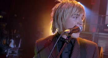 Movie still from “Just My Luck” (2006), directed by Donald Petrie – A man with blonde hair is singing into a microphone; Close Up shot, Over the shoulder angle