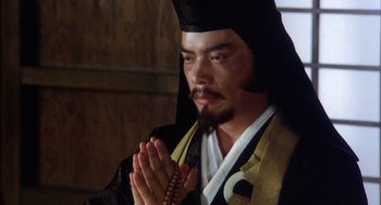 Movie still from “Kagemusha” (1980), directed by Akira Kurosawa – A man in a black hat and a black robe praying; Close Up shot, Low angle