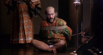 Movie still from “Kagemusha” (1980), directed by Akira Kurosawa – A man with a bald head tied to a rope; Medium shot, High angle