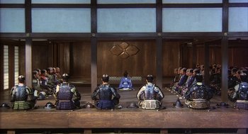 Movie still from “Kagemusha” (1980), directed by Akira Kurosawa – A group of men sitting on a bench in front of an audience; Extreme Wide shot, High angle