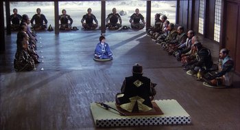 Movie still from “Kagemusha” (1980), directed by Akira Kurosawa – A group of people sitting in a circle and a person sitting on a mat; Extreme Wide shot, High angle