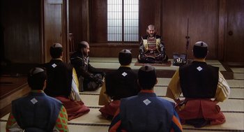 Movie still from “Kagemusha” (1980), directed by Akira Kurosawa – A group of men sitting in a circle in front of each other; Wide shot, High angle