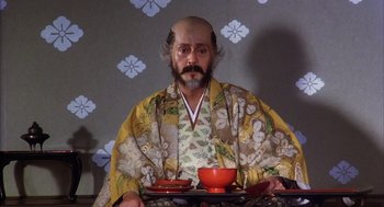 Movie still from “Kagemusha” (1980), directed by Akira Kurosawa – A man in a kimono sitting on a chair with a tray of food; Medium shot, Low angle