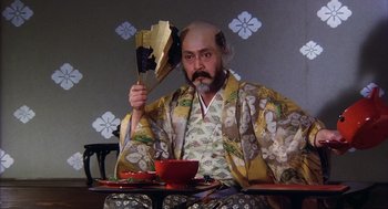 Movie still from “Kagemusha” (1980), directed by Akira Kurosawa – A man with a beard and a hat on holding a knife and fork; Medium shot, Low angle