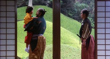 Movie still from “Kagemusha” (1980), directed by Akira Kurosawa – A man holding a young child in his arms while standing next to another man; Wide shot, Over the shoulder angle