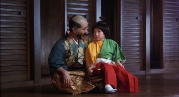 Movie still from “Kagemusha” (1980), directed by Akira Kurosawa – A man sitting next to a little girl wearing a kimono; Medium shot, Low angle