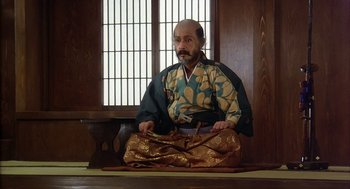 Movie still from “Kagemusha” (1980), directed by Akira Kurosawa – A man sitting on the ground wearing a kimono; Medium shot, High angle