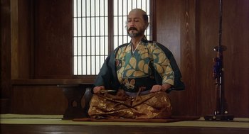 Movie still from “Kagemusha” (1980), directed by Akira Kurosawa – A man in a kimono sitting on the ground with his eyes closed; Medium shot, High angle