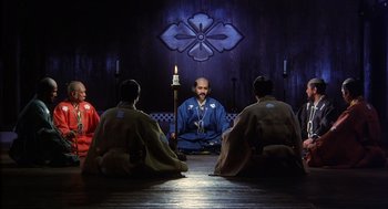 Movie still from “Kagemusha” (1980), directed by Akira Kurosawa – A group of men sitting in a circle around a candle; Wide shot, Low angle