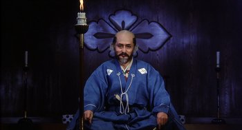 Movie still from “Kagemusha” (1980), directed by Akira Kurosawa – A man in a blue robe sitting in a chair; Medium shot, Low angle