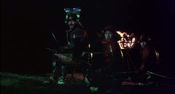 Movie still from “Kagemusha” (1980), directed by Akira Kurosawa – A man and a woman dressed in costume sitting next to a fire; Wide shot, High angle