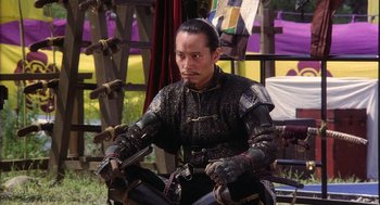 Movie still from “Kagemusha” (1980), directed by Akira Kurosawa – A man in a black and gold outfit sitting on a chair; Medium shot, High angle