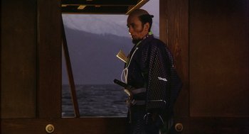 Movie still from “Kagemusha” (1980), directed by Akira Kurosawa – A man standing in front of the ocean holding a sword; Medium shot, Low angle