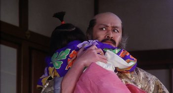 Movie still from “Kagemusha” (1980), directed by Akira Kurosawa – A man holding a doll in his arms and wearing a wig; Close Up shot, Low angle