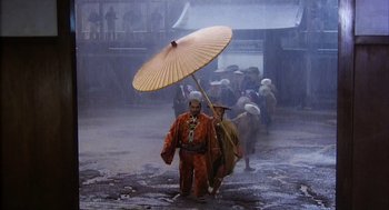 Movie still from “Kagemusha” (1980), directed by Akira Kurosawa – A group of people walking in the rain under an umbrella; Wide shot, High angle