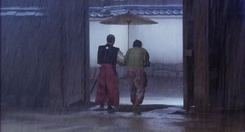 Movie still from “Kagemusha” (1980), directed by Akira Kurosawa – Two people walking in the rain under an umbrella; Wide shot, Low angle