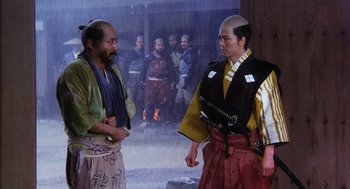 Movie still from “Kagemusha” (1980), directed by Akira Kurosawa – Two men in oriental garb talking to each other in front of a crowd; Medium shot, Over the shoulder angle