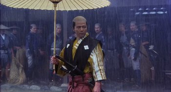 Movie still from “Kagemusha” (1980), directed by Akira Kurosawa – A man holding an umbrella while standing in the rain; Medium shot, Low angle