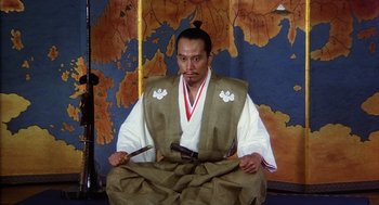 Movie still from “Kagemusha” (1980), directed by Akira Kurosawa – A man sitting in front of a map holding a sword; Medium shot, High angle