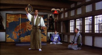 Movie still from “Kagemusha” (1980), directed by Akira Kurosawa – A man holding a fan in front of two other men; Wide shot, Low angle