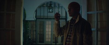 Movie still from “Keanu” (2016), directed by Peter Atencio – A man holding something in his hand while standing in front of a building; Medium shot, Low angle