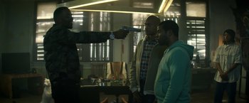 Movie still from “Keanu” (2016), directed by Peter Atencio – A man pointing a gun at two other men in a room; Medium shot, Over the shoulder angle