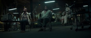 Movie still from “Keanu” (2016), directed by Peter Atencio – A man sitting on a chair in front of a group of people; Wide shot, High angle