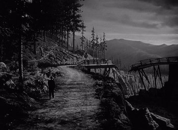 Movie still from “Keeper of the Flame” (1942), directed by George Cukor – A person walking down a dirt road near a forest; Extreme Wide shot, High angle