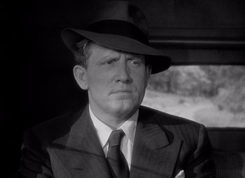 Movie still from “Keeper of the Flame” (1942), directed by George Cukor – A man wearing a suit and a hat in front of a window; Close Up shot, Low angle