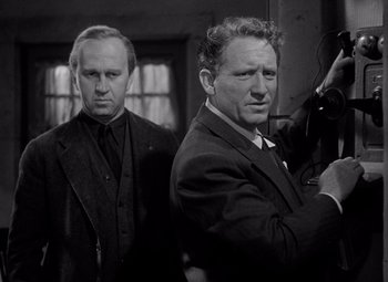 Movie still from “Keeper of the Flame” (1942), directed by George Cukor – A black and white photo of two men in suits and ties; Medium shot, Low angle